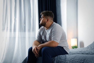 Depressed overweight man on bed at home - obrazy, fototapety, plakaty