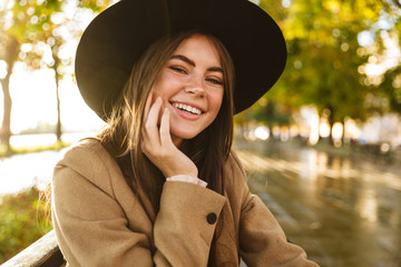 Portrait of caucasian young brunette woman sitting on bench in autumn park