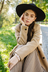 Image of beautiful woman sitting on bench in green park outdoors