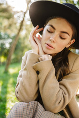 Image of alluring woman sitting on bench in green park outdoors