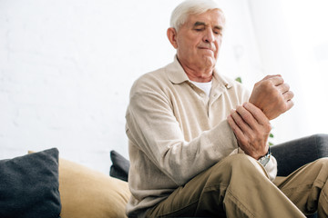 low angle view of senior man sitting on sofa and having pain in hand in apartment