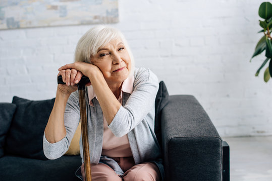 smiling senior woman with wooden cane looking at camera in apartment