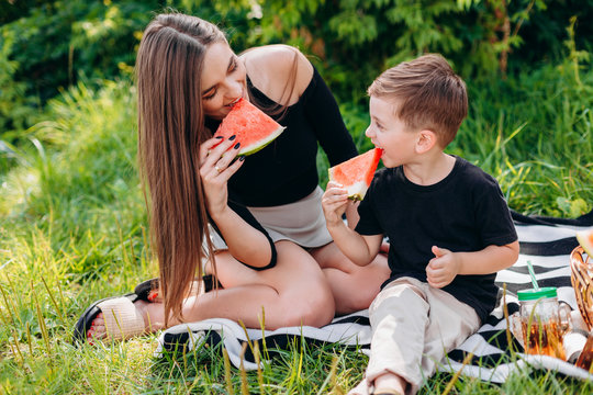 Mother and son  having a picnic in the park are eating a watermelon. - Image