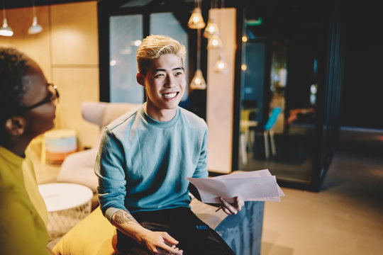 Happy blonde asian hipster guy smiling during conversation wit african american couch talking about coursework, cropped image of multiracial colleagues having conversation about project in office