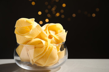 Uncooked pappardelle pasta on grey table against blurred lights