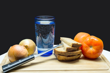 Bread, onions, tomatoes, a knife and water in a glass