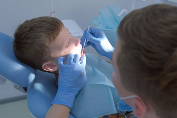 Dentist making fluoridation of child boy teeth after cleaning for protection. Doctor hygienist...
