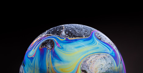 close up of a colorful soap bubble isolated on a black background, looking like a planet in space.