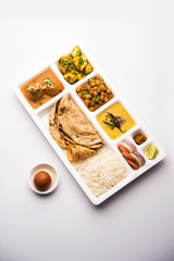 Indian vegetarian Food Thali or Parcel food-tray with compartments in which Malai Kofta, chole, Dal tarka, dry aloo sabji, chapati and rice with sweet gulab jamun served