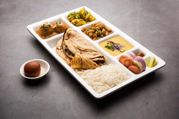 Indian vegetarian Food Thali or Parcel food-tray with compartments in which Malai Kofta, chole, Dal tarka, dry aloo sabji, chapati and rice with sweet gulab jamun served