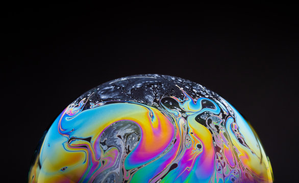 close up of a colorful soap bubble isolated on a black background, looking like a planet in space.