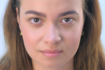 Portrait of beautiful young girl before beauty procedure of permanent eyeliner in cosmetology clinic. Face closeup view. Woman is looking at camera on white background, front view.