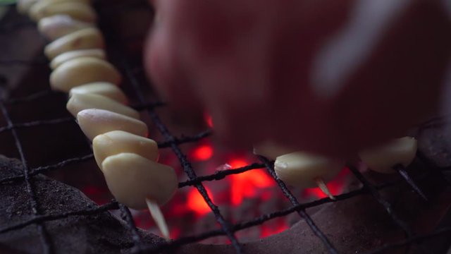 Peeled garlic getting grill on charcoal grill. hot fire under. flip it. burnt.