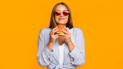 Stylish Millennial Girl Smelling Burger Standing In Studio, Panorama