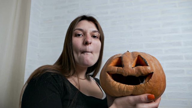 A young girl holds a missing pumpkin in her hands and wrinkles her face, makes various facial expressions. Pumpkin image