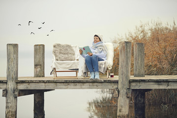 ältere Frau mit Buch am Steg am See mit warmen Fell im Winter