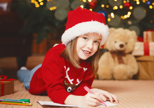 Smiling little girl in xmas hat writing letter to Santa