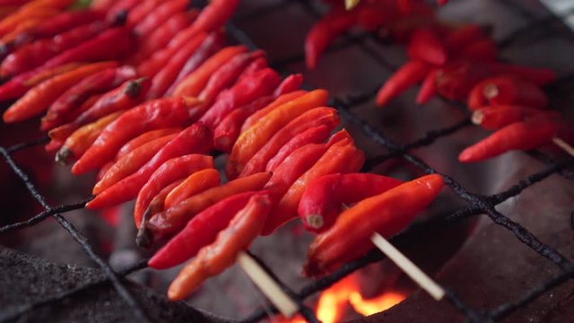 Red chilli with skewer getting grill on a charcoal grill. Flip with old lady hand.