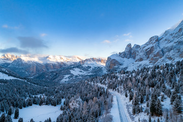 Fototapeta na wymiar Aerial view of Curved road in the snowy mountains of Italian Alps in South Tyrol with dolomites in background / Sunny winter day with harsh shadows and lot of snow