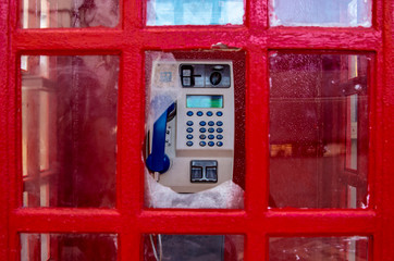 Tradycyjna czerwona budka telefoniczna, nowoczesny aparat telefoniczny, zbita szyba. - obrazy, fototapety, plakaty