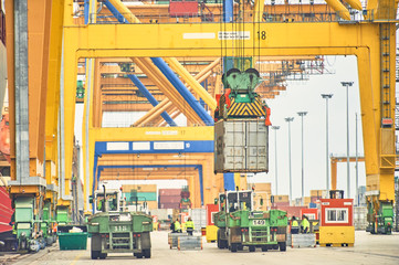 Container handling gantry crane loading container trucks along port dock. Maritime transportation infrastructure and shipping logistics. Export and import bussines