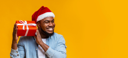 Joyful black man in santa hat shaking christmas gift box