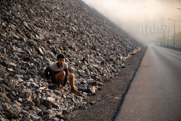 alone man sitting down on rocks with asphalt road and foggy background