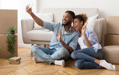 Obraz premium Happy Couple Taking Selfie Gesturing Victory Sign After Moving House