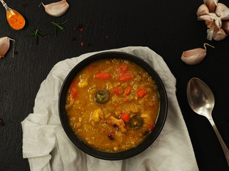 Traditional pea soup with meat, carrots, paprika and turmeric. Soup on a black stone background, next to cloves of garlic, sprigs of rosemary and turmeric. Flat lay. Natural lighting.