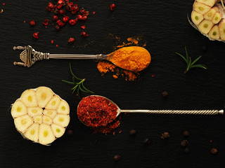 Top view of oriental spices on a black stone background. Spices in and around vintage teaspoons on a black table. Cut across the head of garlic. Flat lay.