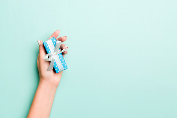 Woman hands give wrapped christmas or other holiday handmade present in colored paper. Present box, decoration of gift on Blue table, top view with copy space