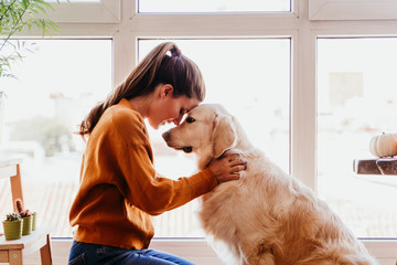 close up of beautiful woman hugging her adorable golden retriever dog at home. love for animals concept. lifestyle indoors - 303891953