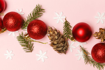 Obraz na płótnie Canvas Red Christmas shiny balls and fir twigs on pale pink background. Christmas ornaments arrangement.