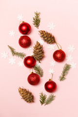 Red Christmas shiny balls and fir twigs on pale pink background. Christmas ornaments arrangement.