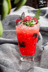 Glass with strawberry mojito cocktail with lemon and mint, cold refreshing drink or beverage with ice on gray background. Overhead view, copy space. Advertising for cafe menu. Vertical photo.