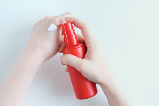 Red Plastic Bottle With Hand Cream In The Hands Of A Caucasian Girl. View From Above.