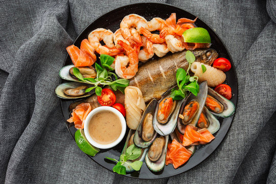 Roasted Mixed Seafood Contain Mussels, prawns, salmon, Calamari Squids and Grilled Barracuda Fish Garlic with Spicy Chili Sauce. Isolated on gray Background. Seafood and meat platter. Horizontal