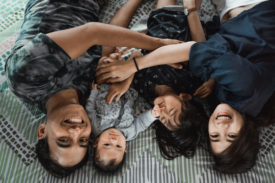 Asian young family lying with embrace on the bed and smile looking up to the camera