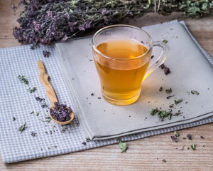 Warm oregano tea in a glass cup stands on linen beige napkins on the background of dry oregano.