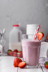 Strawberry protein shake on a white wooden background. Fresh milkshake with strawberries on a light table. A glass of strawberry smoothie.