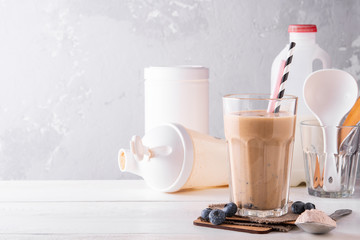 Chocolate protein shake on a white wooden background. Fresh milkshake with blueberry on a light table. A glass of chocolate smoothie . - obrazy, fototapety, plakaty