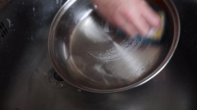 Washing a pot by hand in a stainless steel sink