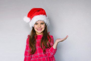 happy funny child girl in red Christmas hat on gray background.
