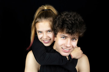 Brother and sister have fun together, the girl hugs her brother and together they laugh at the dark background. The guy with dark hair and the girl with blond hair