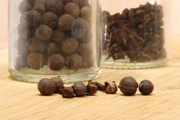 Spices pepper peas and cloves on a wooden table on a background of glass jars 