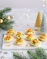 Canapes with smoked salmon, cream cheese and avocado on light background with space for text. Christmas and new year holidays background concept. Starters snacks recipe ideas.