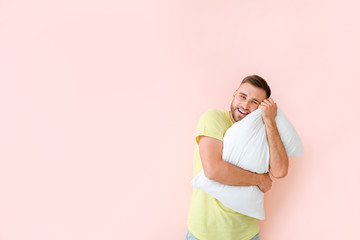 Young man with pillow on color background