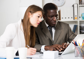 Young  woman and man colleagues working with laptop and papers