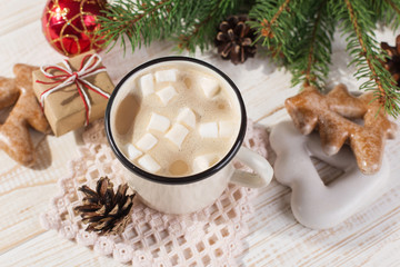 Obraz na płótnie Canvas Hot Christmas drink with marshmallows in an iron mug and gingerbread cookies, on a white table. New Year, holiday background, copy space.