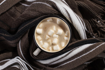 Fototapeta na wymiar Hot Christmas drink with marshmallows in an iron mug, on a wooden table and a scarf. New Year, holiday background, greeting card copy space.